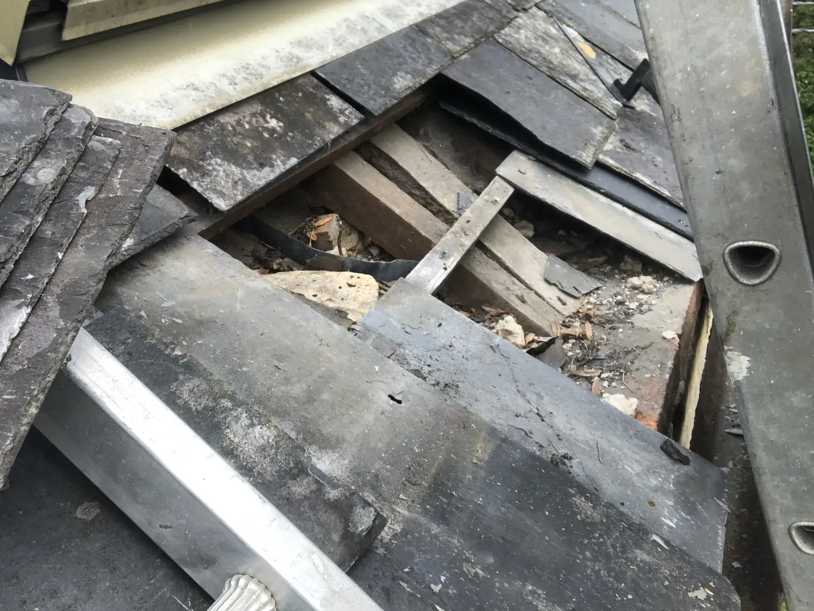 Storm-damaged slate roof opening beside the existing roof-window flashing