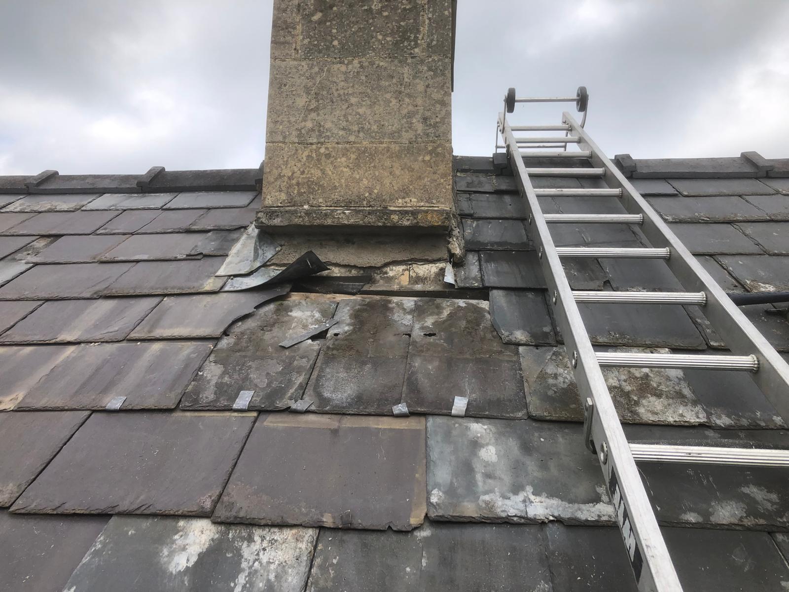 Missing slates and exposed roof area below a chimney before repair