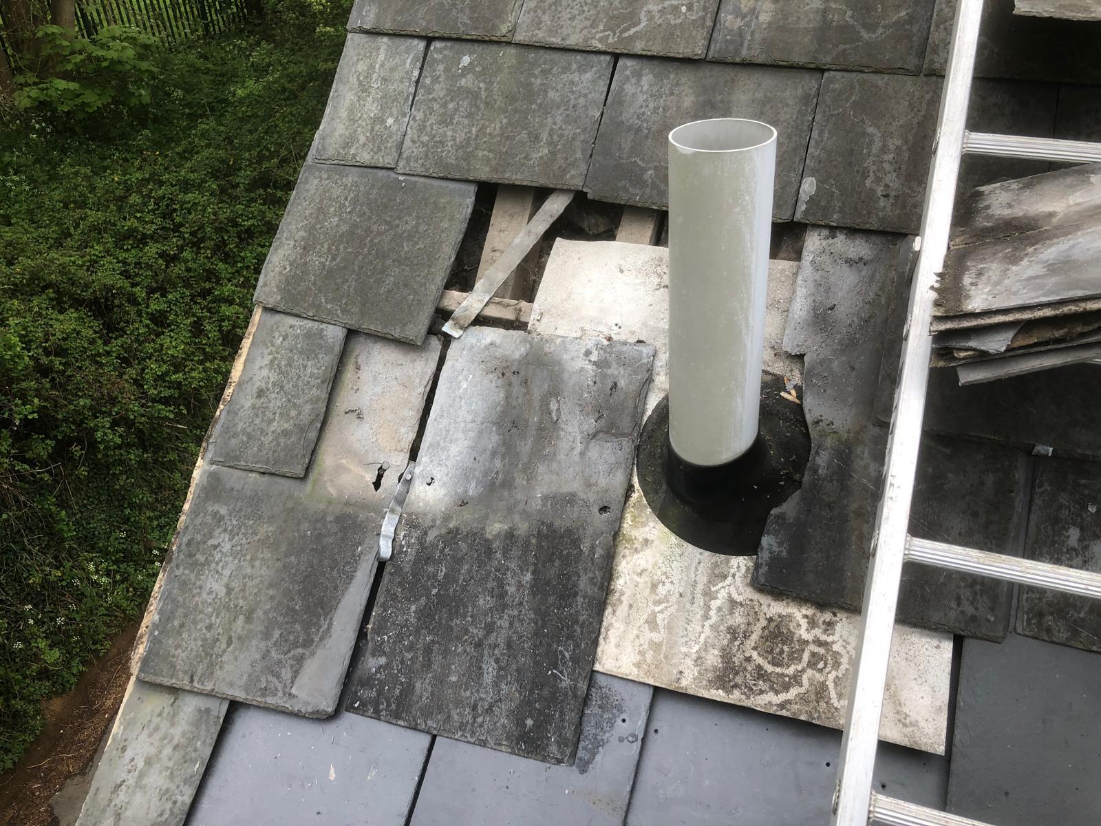 Broken and missing slates exposing the roof beside a newly installed boiler flue