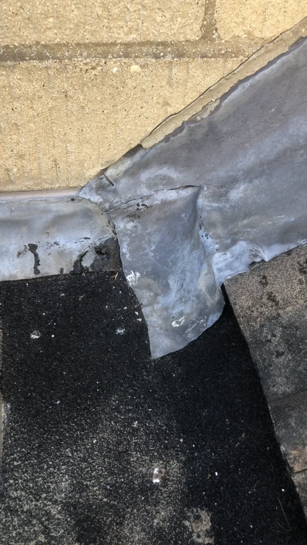 Split and lifted leadwork at the junction of a bituminous flat roof, tiled pitched roof and house wall